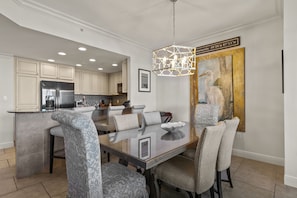 A modern kitchen with white cabinets, a stainless steel refrigerator, and a dining area with a glass table and upholstered chairs.
