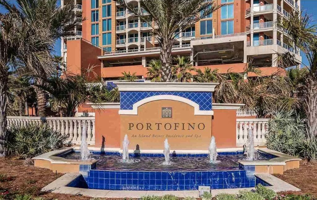 Entrada de un hotel con una fuente, palmeras y un edificio de varios pisos al fondo.