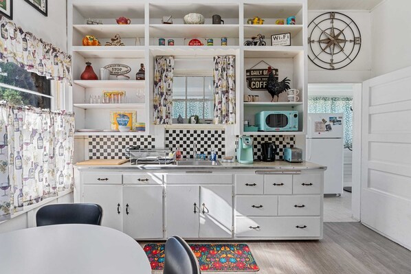 A kitchen with white cabinets, a checkered backsplash, a microwave, and various kitchen items on shelves.
