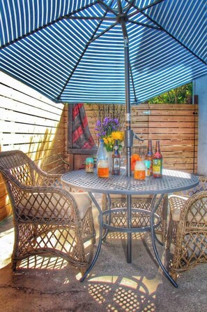 A round metal table with wicker chairs, an umbrella, and bottles of beer.