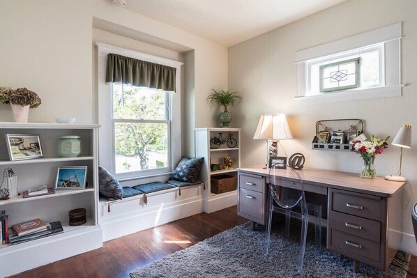 A room with a desk, shelving, a window seat, and a view of greenery.