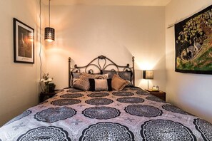 Een net opgemaakt bed met een bedsprei met dessin, een wandlamp, een ingelijste foto en een wandtapijt.