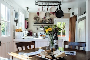 A kitchen with hanging pots, a dining table with bread and cheese, and a vase with flowers. - Historic Santa Rosa Cottage Hot Tub (Santa Rosa)