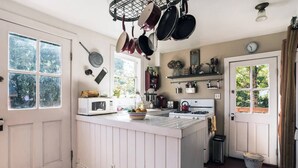 Une cuisine dotée d’un îlot central, d’un four à micro-ondes, d’une bouilloire et de casseroles suspendues.