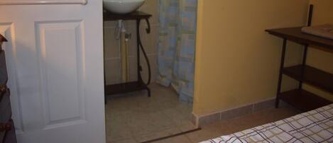 A small bathroom with a white door, a sink, a shower curtain, and a shelf.