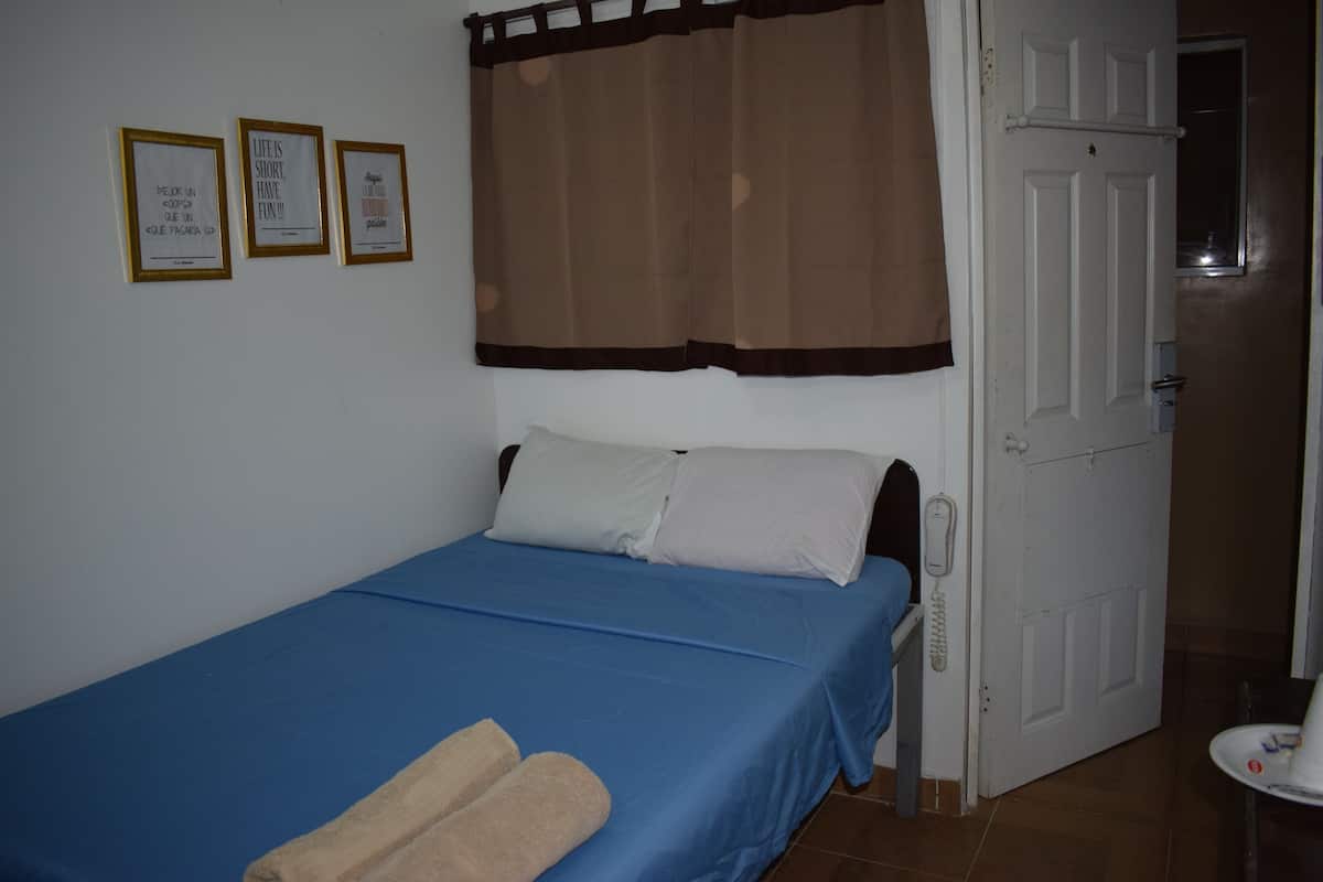 A single bed with a blue bedspread, two pillows, and a pair of towels. There are three framed pictures on the wall.