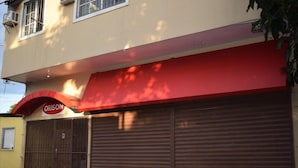 A building with a red awning and a closed metal shutter door. - Orison Managua (Managua)