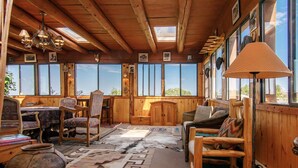 A rustic cabin interior with wooden walls, large windows, a dining area, and a cozy seating area. - Rustic Ranch Retreat (Lamy)