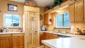 A kitchen with wooden cabinets, a large window, and a door with a 'Shilling' sign. - Rustic Ranch Retreat (Lamy)