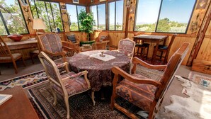 A wooden interior with a round table, chairs, and a view through large windows. - Rustic Ranch Retreat (Lamy)