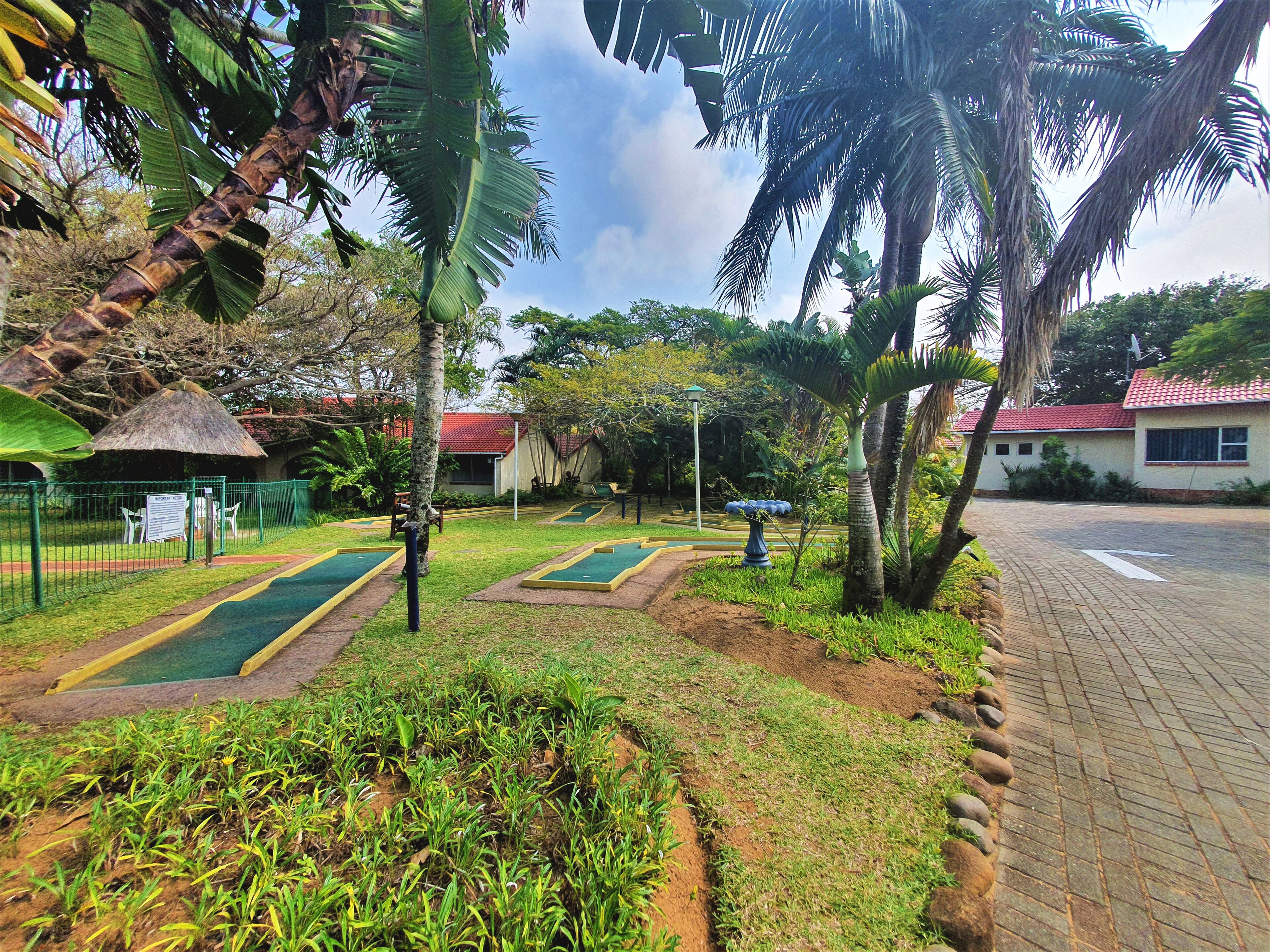 Ein Golfplatz mit grünen Spielbahnen, einem Pavillon mit Strohdach und einem Gebäude mit rotem Dach.