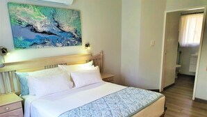 A neatly made bed with a quilt, a bedside table, and a nightstand. There is a painting on the wall above the bed.