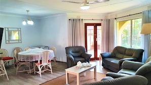 A living room with a dining area, a ceiling fan, and a view through a glass door.