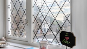 Une fenêtre ornée d’une grille à motifs losangés, une tasse, un livre et une pancarte sur laquelle on peut lire « J’adore la bière ».