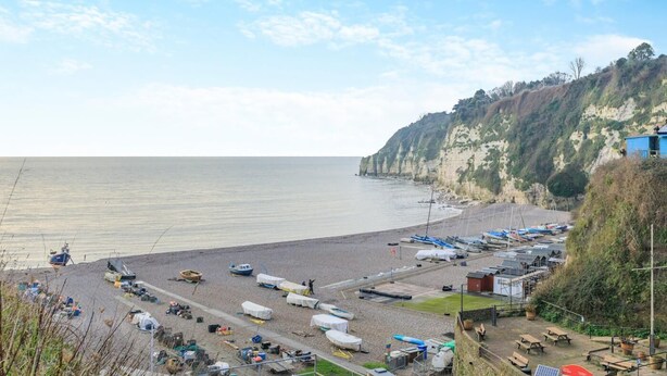 Une zone côtière où se trouvent des bateaux amarrés, une plage et une falaise couverte de végétation.