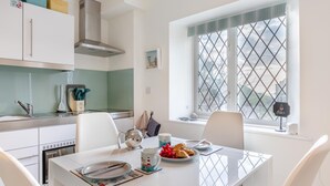 Une cuisine moderne avec des armoires blanches, une hotte de cuisinière en acier inoxydable et une fenêtre dotée d’un store à motifs losangés.