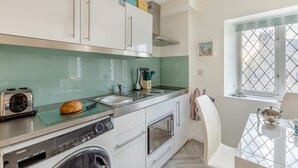 Une cuisine moderne avec des meubles blancs, un plan de travail en acier inoxydable, un grille-pain, une miche de pain, un évier et une fenêtre donnant sur un beau paysage.