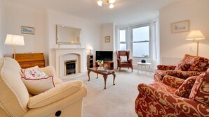 Een woonkamer met een open haard, een televisie, een bank, een fauteuil en een lamp.