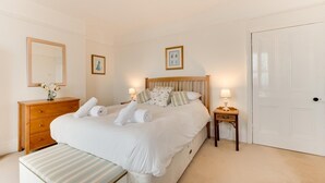 Een slaapkamer met een bed, nachtkastjes, een dressoir, een bankje en een deur.