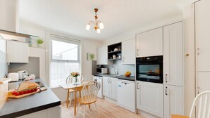 Een moderne keuken met witte kastjes, een eettafel, stoelen, een kroonluchter en uitzicht op de stad.