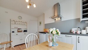 Een keuken met witte kastjes, een houten eettafel, een klok en een bloevas.