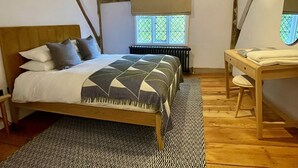 A bedroom with a wooden bed, a bedside table with a mirror, a radiator, and a window with a view. - Coventry Historic Houses (Coventry)