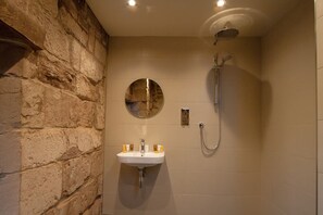 A bathroom with a stone wall, a round mirror, a sink, and a shower. - Coventry Historic Houses (Coventry)