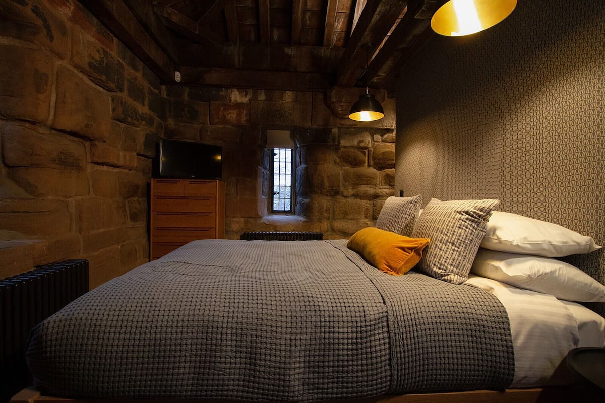 A bedroom with a stone wall, a wooden bed, a television, and a window.