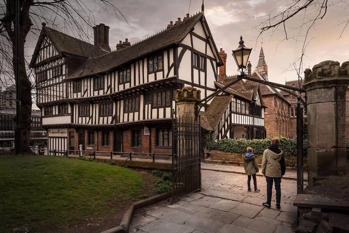 A traditional Tudor-style building with a gated entrance, stone pillars, and a cobblestone pathway.