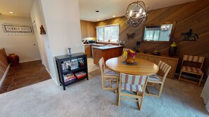 A cozy dining area with a wooden table and chairs, a bookshelf, and a kitchen in the background.