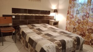 A bedroom with a large bed, a chair, a nightstand, a lamp, and a decorative wall piece.