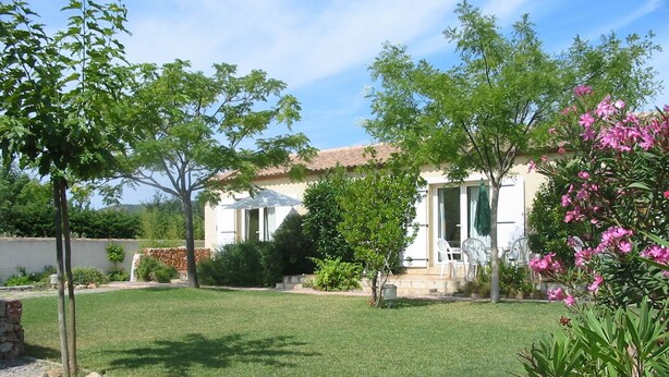 A house with a patio, a lawn, and a garden with pink flowers.