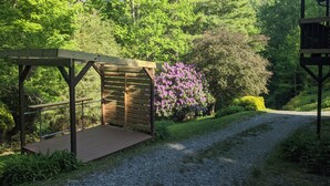 A wooden pergola with a gravel path leading to it, surrounded by lush greenery and a variety of trees. - Country road take me home! (Boone)