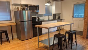 A modern kitchen with stainless steel appliances, a wooden table, and bar stools. - Country road take me home! (Boone)