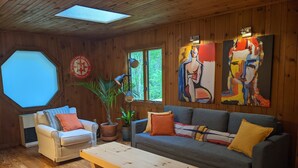 A cozy living room with a wooden interior, a sofa, a coffee table, and two chairs. There are two windows, a potted plant, and a painting on the wall. - Country road take me home! (Boone)