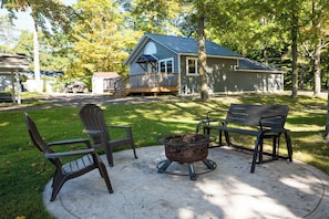 A backyard with a fire pit, two Adirondack chairs, and a house with a blue roof. -  Lake Metonga Cabin (Crandon)
