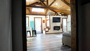 A spacious living room with a high ceiling, wooden beams, a fireplace, a television, and a sofa.