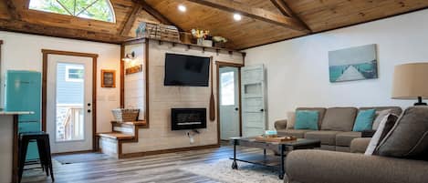A spacious living area with a wooden ceiling, a flat-screen TV mounted on a wall, a sofa set, and a coffee table.