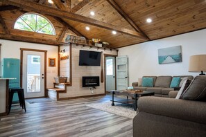 A spacious living area with a wooden ceiling, a flat-screen TV mounted on a wall, a sofa set, and a coffee table. -  Lake Metonga Cabin (Crandon)