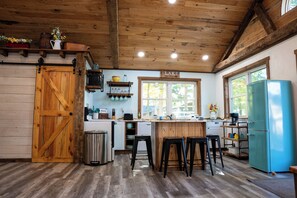 A rustic kitchen with wooden beams, a farmhouse door, a vintage blue refrigerator, and a window with a view of trees. -  Lake Metonga Cabin (Crandon)
