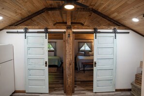 A loft-style room with a high ceiling, exposed wooden beams, and a central wooden beam supporting a sliding barn door. -  Lake Metonga Cabin (Crandon)