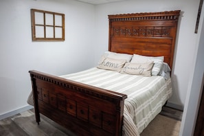 A bedroom with a wooden bed, a headboard with decorative elements, and a window with a wooden frame. -  Lake Metonga Cabin (Crandon)