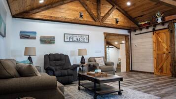 A cozy living room with wooden beams, a sofa, two armchairs, a coffee table, and a welcome sign.