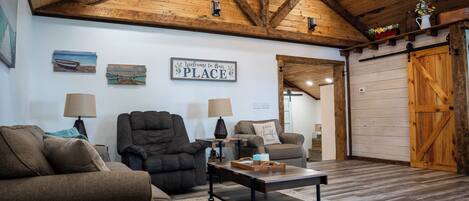 A cozy living room with wooden beams, a sofa, two armchairs, a coffee table, and a welcome sign.