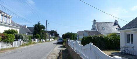 A narrow street lined with white houses, a parked car, and a white fence along the side.