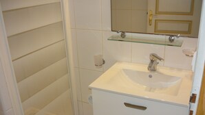 Un bagno con un lavandino bianco, uno scaffale in vetro e uno specchio sopra il lavandino.