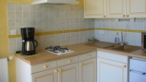Una cucina con mobili bianchi, un piano cottura a gas, una macchina da caffè e un backsplash in piastrelle gialle.