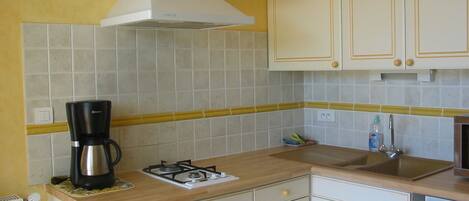 Una cocina con armarios blancos, estufa a gas, cafetera y salpicadero de azulejos amarillos.