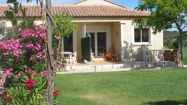Una casa con tetto in tegole, un portico coperto con mobili da esterno e un prato.