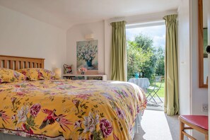 Une chambre avec un grand lit, une table de chevet avec une lampe, un tableau au mur et une vue sur le jardin par la fenêtre.